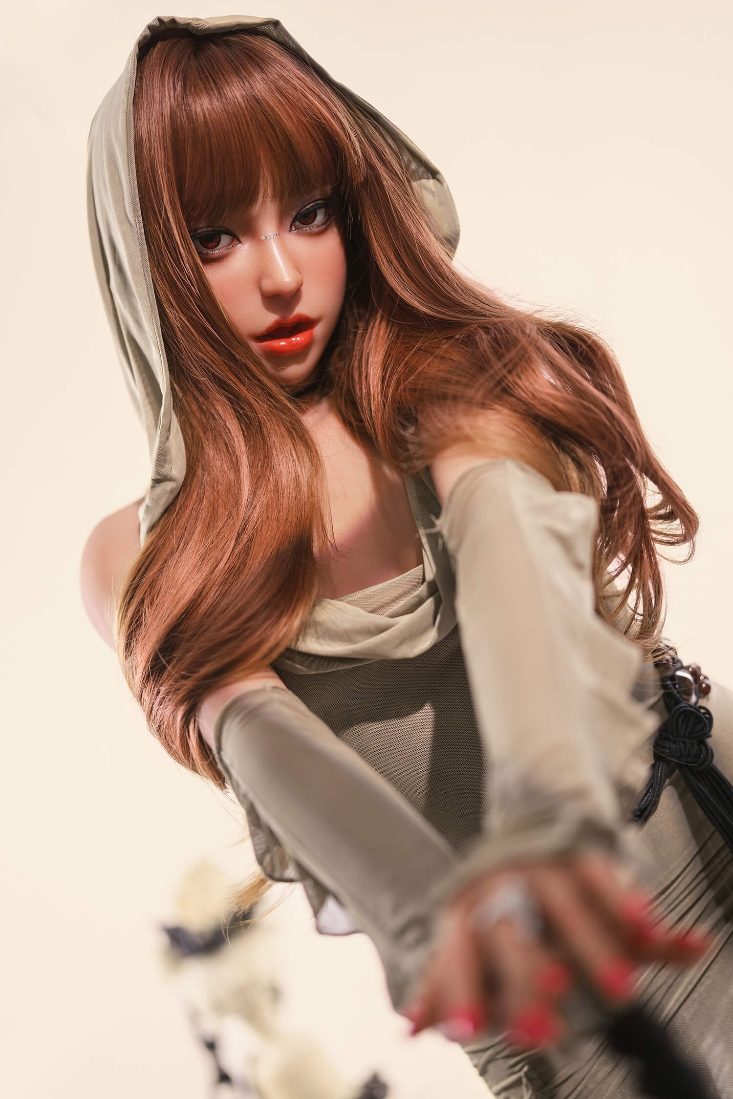 Portrait of a young woman with long brown hair wearing a beige hooded outfit, gazing at the camera against a pale background.