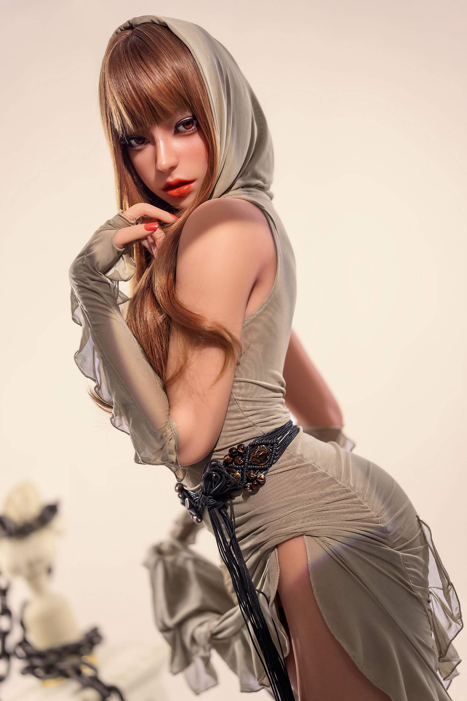 Model in a beige hooded outfit posing sideways with long hair, red lipstick, and a beaded belt