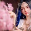 Cosplay portrait of an elf-like woman with blue hair, ornate headpiece, and dangling chains among pink blossoms in the foreground.