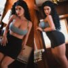 Split image of a woman with curly hair in a blue crop top and black mini skirt posing by wooden walls; left leaning on a door frame, right standing with hand on a wall.