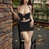 Woman in a black halter dress with heart cutouts poses beside a brick pillar outdoors.