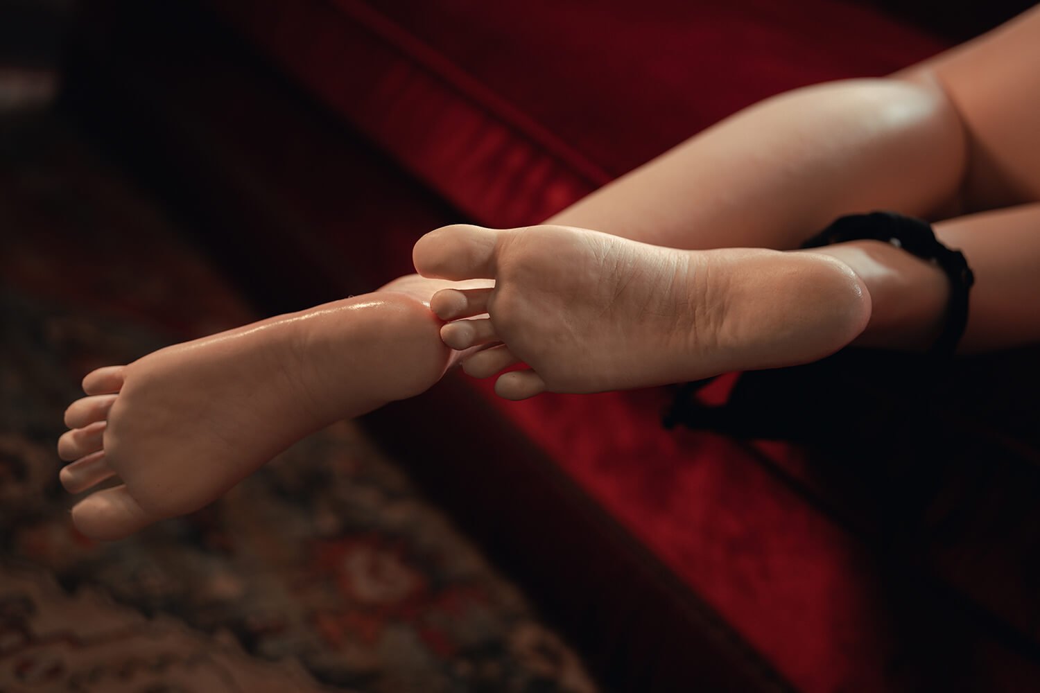 Two bare feet resting together, one foot lying atop the other on a dark red background.