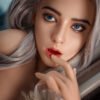 Close-up portrait of a woman with striking blue eyes and silver hair, soft makeup, and a finger resting near her lips.