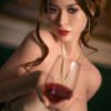 Close-up of a woman in a beige bikini top, holding a wine glass toward the camera, with blue eyes and glossy lips.
