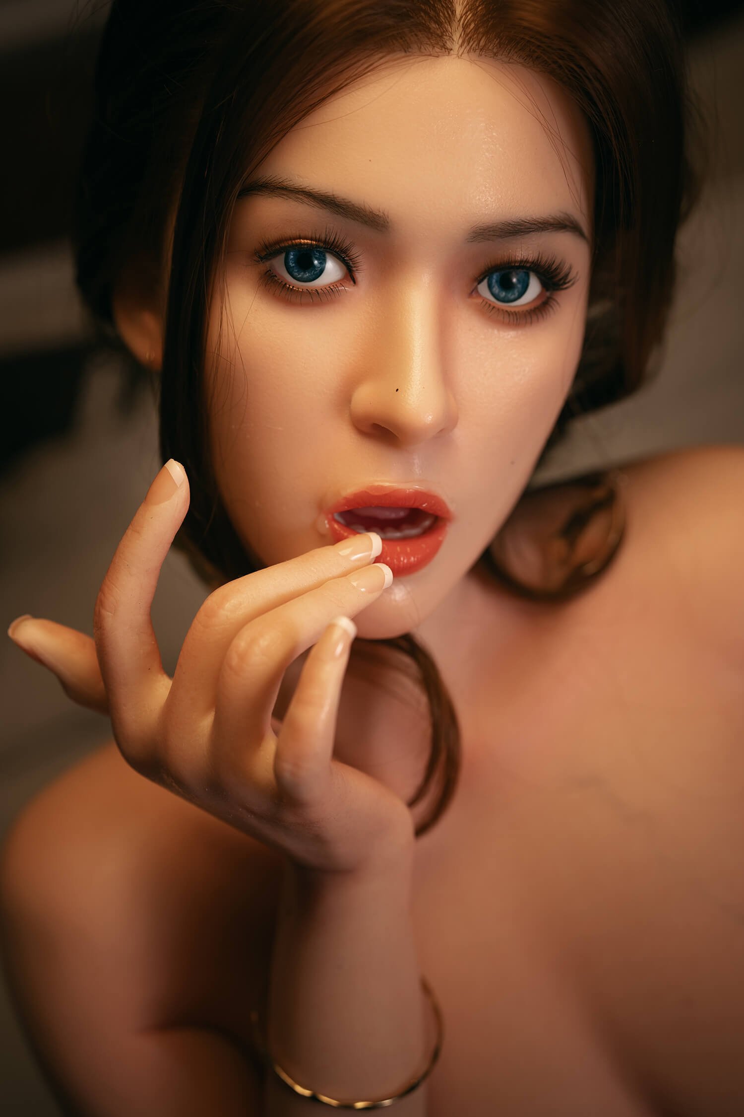 Close-up of a woman with blue eyes and glossy red lips, fingers near her mouth in a contemplative pose.