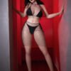Woman in black fishnet lingerie stands in a red-lit hallway, hands against the walls, looking at the camera.