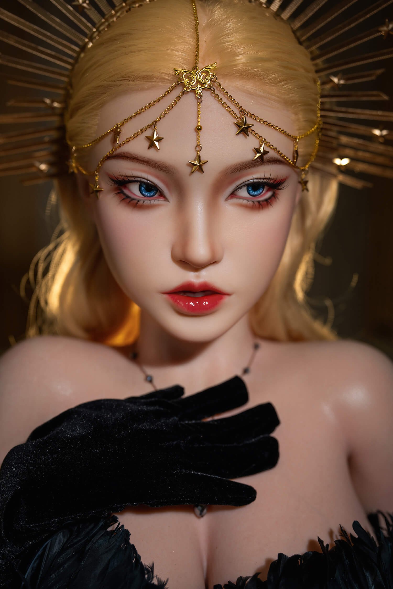 Close-up of a fashion doll with blonde hair and blue eyes, wearing a gold star-spangled headpiece and a black feathered outfit.