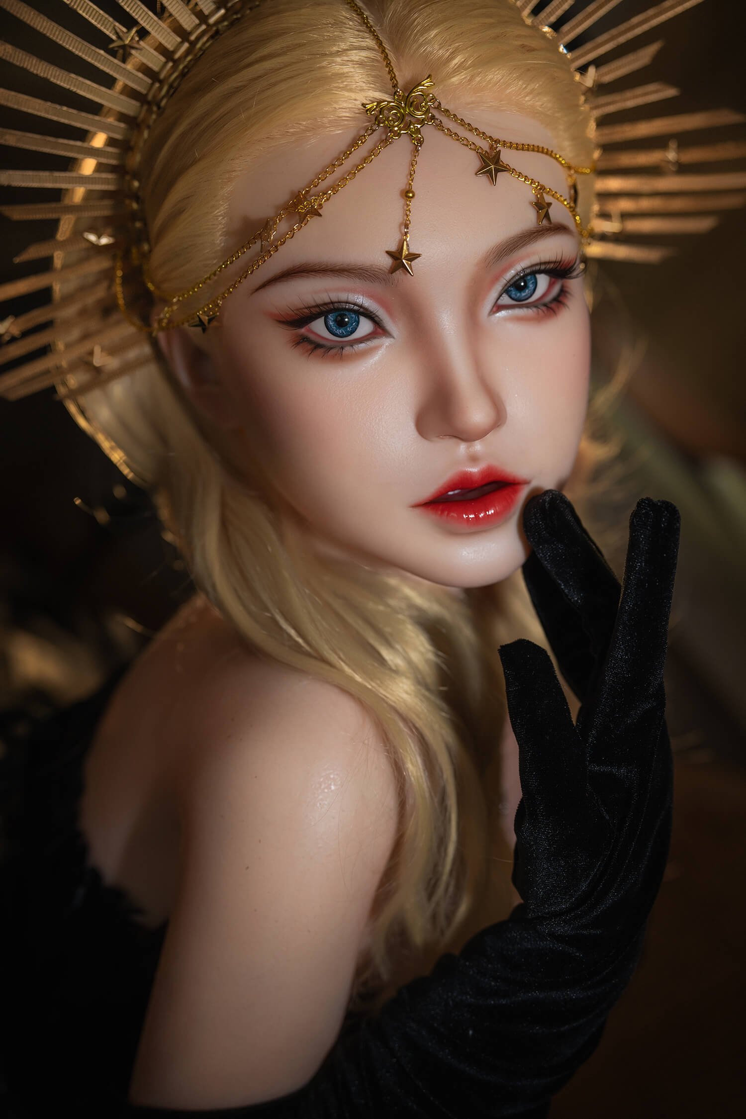 Close-up of a mannequin/doll with blue eyes, red lips, blonde hair, and a gold halo-style headpiece with star charms." ,