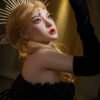 Portrait of a blonde woman wearing a gold sunburst crown, dramatic makeup, and a black velvet sleeve, looking upward.