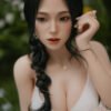 Close-up portrait of a woman with long black hair in a white top, outdoors among greenery, gazing at the camera.