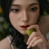 Close-up of a woman with dark hair holding a green grape near her lips, eyes softly looking forward.