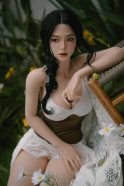 Young woman with long black hair braided over one shoulder sits among greenery and white flowers, wearing a white top and brown skirt.